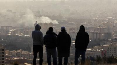 Four men stood on a hill looking at smoke over Tehran
