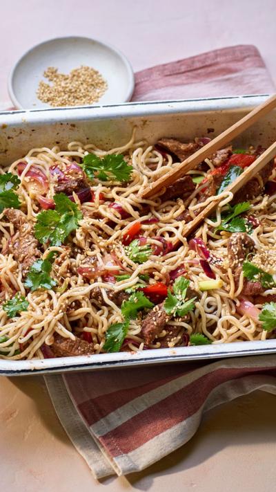 A rectangular baking tray with chilli beef noodles in and a pair of chopsticks sitting on the top