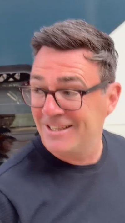 Man with brown hair and glasses wearing navy top at a train station.