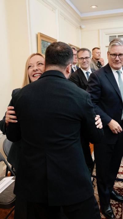 Zelensky hugging Meloni, as Starmer looks on, in the Ukrainian Embassy 