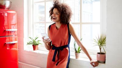Woman stands in the window holding her phone