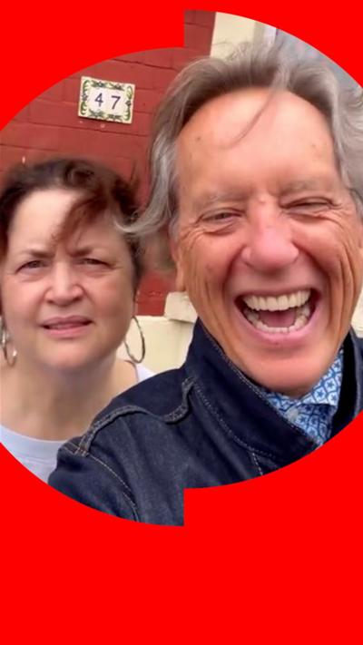Ruth Jones and Richard E Grant smiling at the camera with a terraced house in the background.