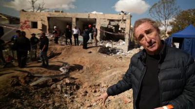 The BBC's Sebastian Usher stands amongst rubble and debris in Dimona in Israel