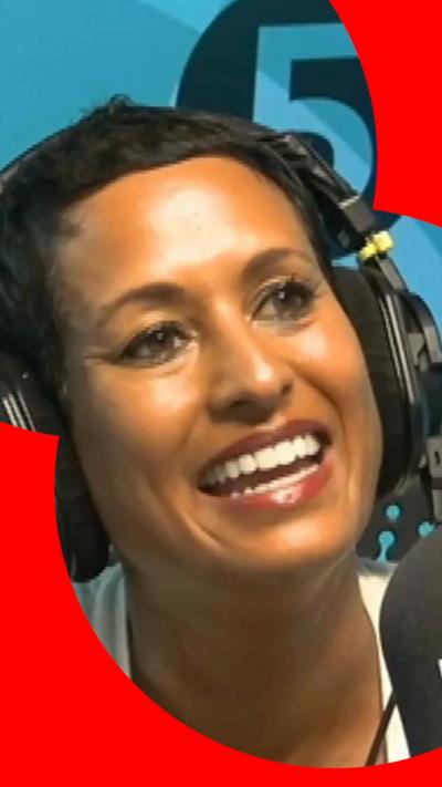 A woman with short, dark hair smiles as she talks into a microphone