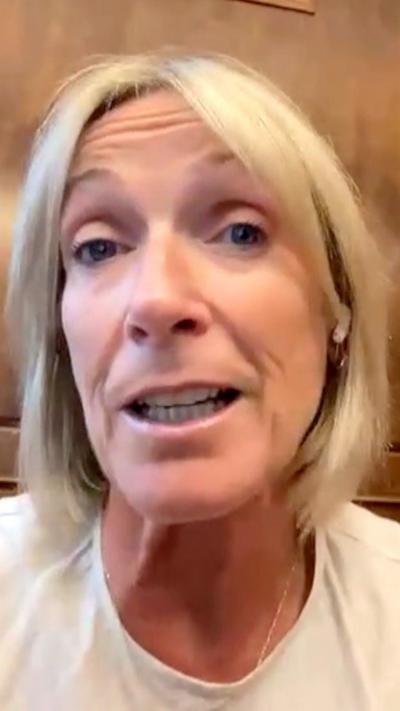 Woman with blonde hair and in a white top talking into the camera with earphones in.