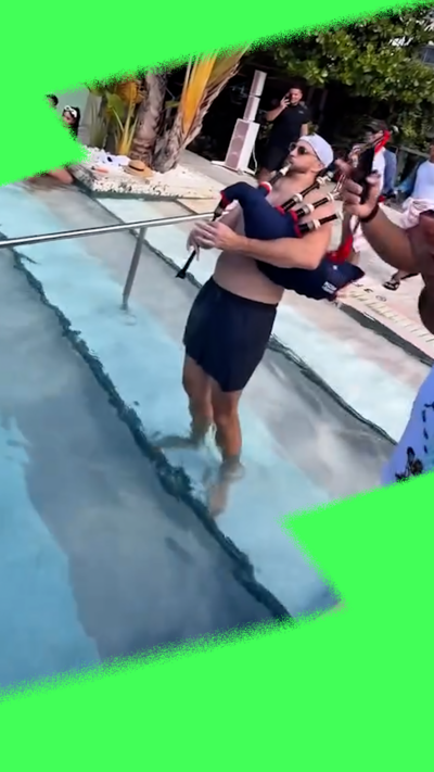 Man in shorts playing bagpipes in front of a pool, with palm trees and hotel behind.