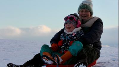 Inbheach agus pàiste air slaodan san t-sneachda an Uibhist agus iad a' cluich còmhla. 