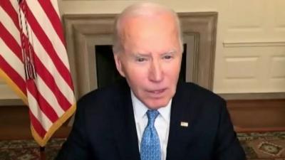 Joe Biden speaking on a virtual call with American flag behind him