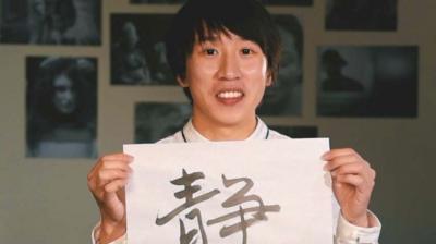 Man holding up a white piece of paper featuring Chinese calligraphy