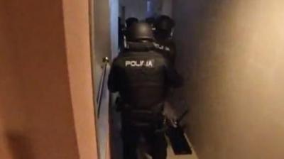 Armed police storm an apartment. They are wearing black clothing with Policia written on it