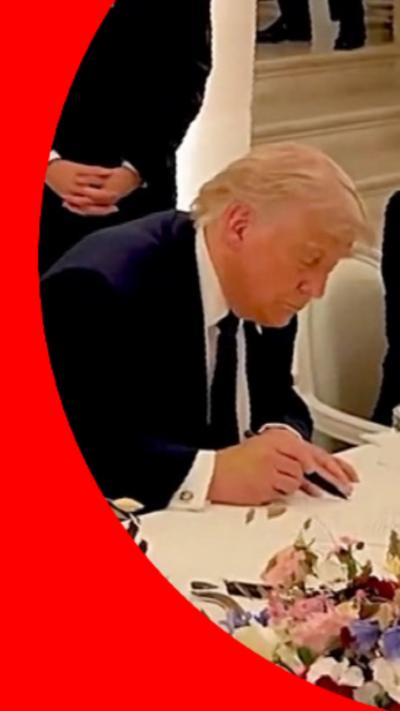 Donald Trump signing a document on a white table.