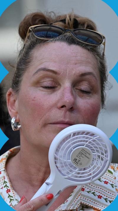 Woman holds a handheld fan to her face and closes her eyes.