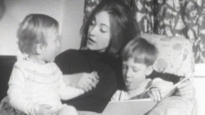 Lynette sitting with her two children, reading them a book.