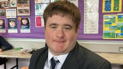 Joshua looking directly at the camera, wearing a school uniform with black blazer and tie