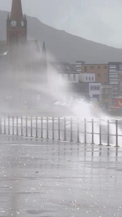 Wave crashes against railings with town in the background