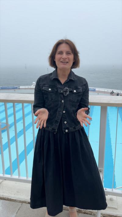 Stephanie Lewis in a denim jacket and blue dress. Behind her is a blue pool.