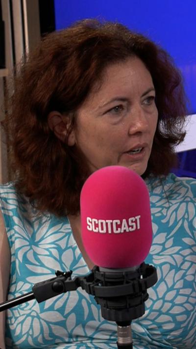 Woman in floral dress in front of microphone with Scotcast written on it.