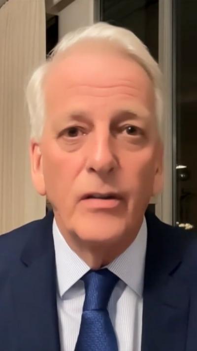 A man in a blue suit and blue tie looks into a camera as he does a virtual interview.