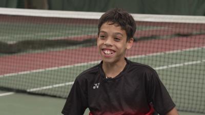 Leo smiling in front a of a tennis net.