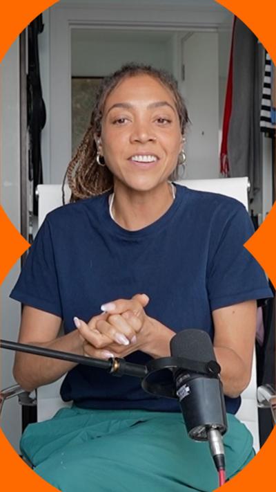 Miquita has tied-back hair and is wearing a blue t-shirt and green trousers sat on a white seat