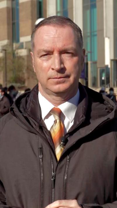 A man wearing a shirt and tie and rain jacket looks towards the camera