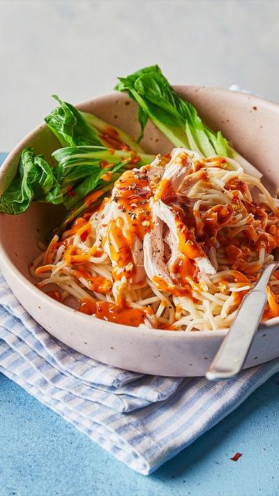 Light coloured bowl on a blue-striped napkin with noodles and veg in it