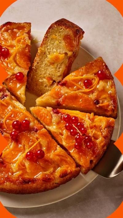 A yellow cake with berries on top, with half cut into slices, on a pink background.
