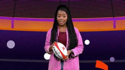 Newsround presenter Emma-Louise in a pink jacket holding a rugby ball