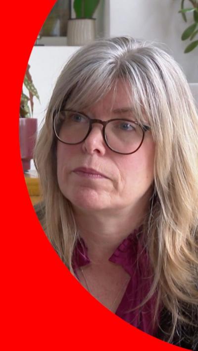 Liz Hopkins, a woman with shoulder length light hair wearing black rimmed glasses looking off camera