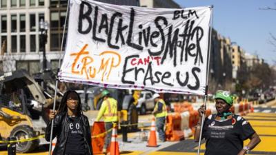 Two women hold up a Black Lives Matter banner in front of construction workers