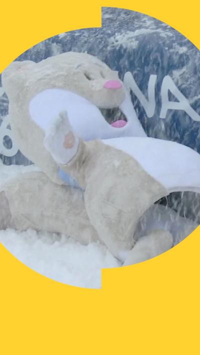 A person dressed as Olympic mascot, Tina - a light coloured stoat - lies in the snow 