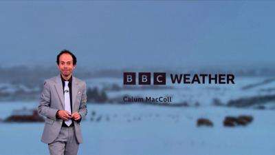 Weather presenter Callum MacColl wears a grey suit and stands in front of greenscreen showing freezing temperatures.