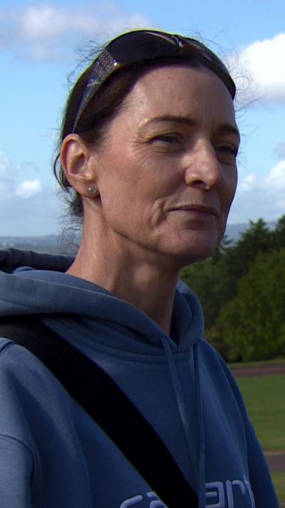 A lady with black hair tied back in a ponytail with glasses on her head wearing a blue hoodie.