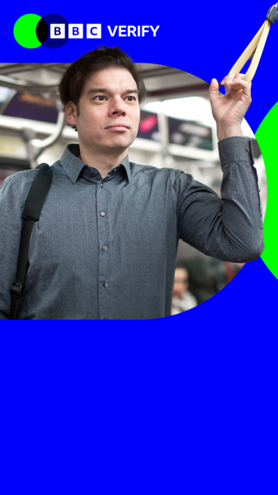 A man holds a handle on a train. He is imposed over the BBC Verify colours and branding. 