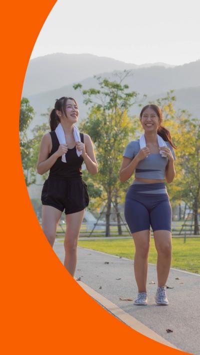 Two women in sports clothes smile while exercising outdoors - they have towels around their necks 