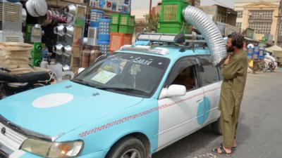 A taxi driver position an air conditioning unit on top of his vehicle.