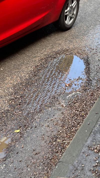 Pothole in the road near to kerb with a red car passing