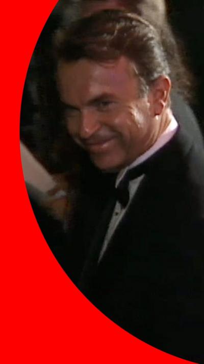 Sam Neill smiling and standing next to his young son during JP premiere in 1993