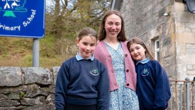 Woman in a pink cardigan with two girls in sweaters on either side