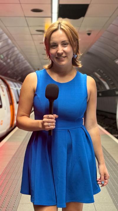 A girl with short ginger hair wearing a blue skater dress stands on the platform inside a Glasgow Subway station with two subways on either side.