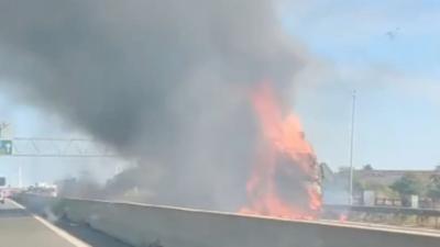 Flames and thick smoke rise from a lorry fire at the side of a major road.
