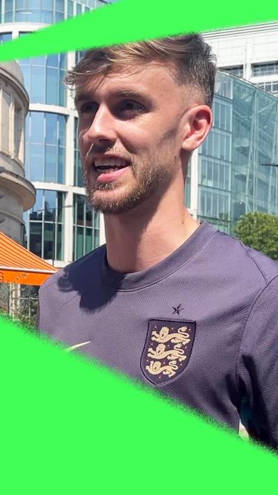 A man speaking to a reporter on a London street, wearing an England training t-shirt and holding a BBC News microphone