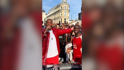 Will Smith holding a microphone besides another man, both wearing red, in front of a crowd.