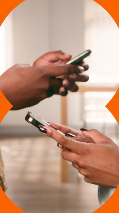 Two people stand facing each, looking down at their phones.