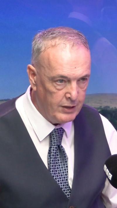 Man with short hair wearing a white shirt, blue tie and a dark blue waistcoat