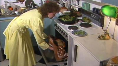 Woman in a yellow dress takes a vegetarian roast out of the oven