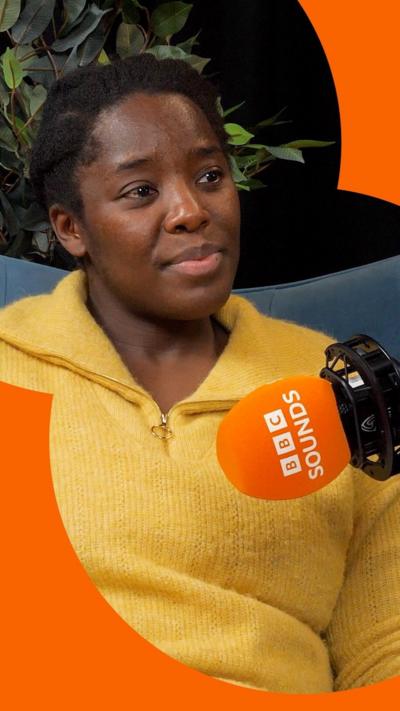 A woman in a yellow jumper, in front of a microphone.