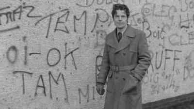 Man stands in front of a wall of graffiti