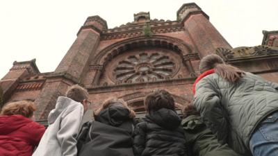 from behind we see children looking up at a stately old building 
