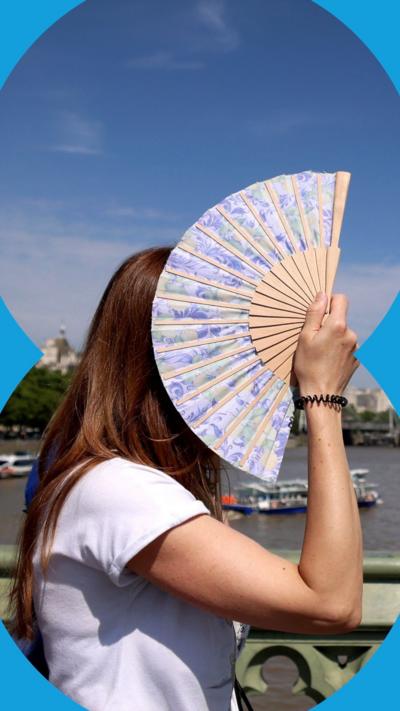A woman with her face covered by her hand-held fan, with the River Thames and London Eye in the background